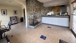 A reception area with a stone wall, a fireplace, a counter with a computer, framed pictures on the wall, and a chair. - Inn at San Luis Obispo (San Luis Obispo)