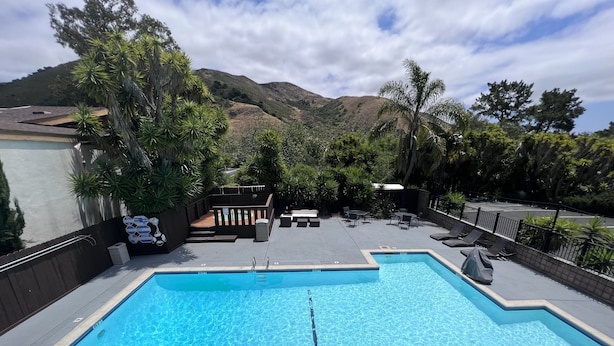 A rectangular swimming pool with clear blue water, surrounded by lounge chairs and a deck area with tables and chairs. - Inn at San Luis Obispo (San Luis Obispo)