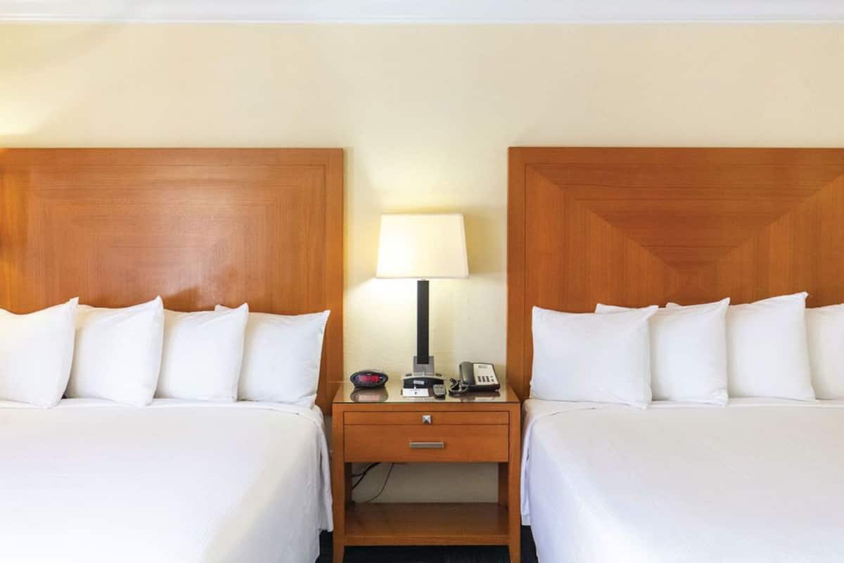Habitación de hotel con dos camas, una mesita de noche con lámpara, teléfono y una pequeña mesa.