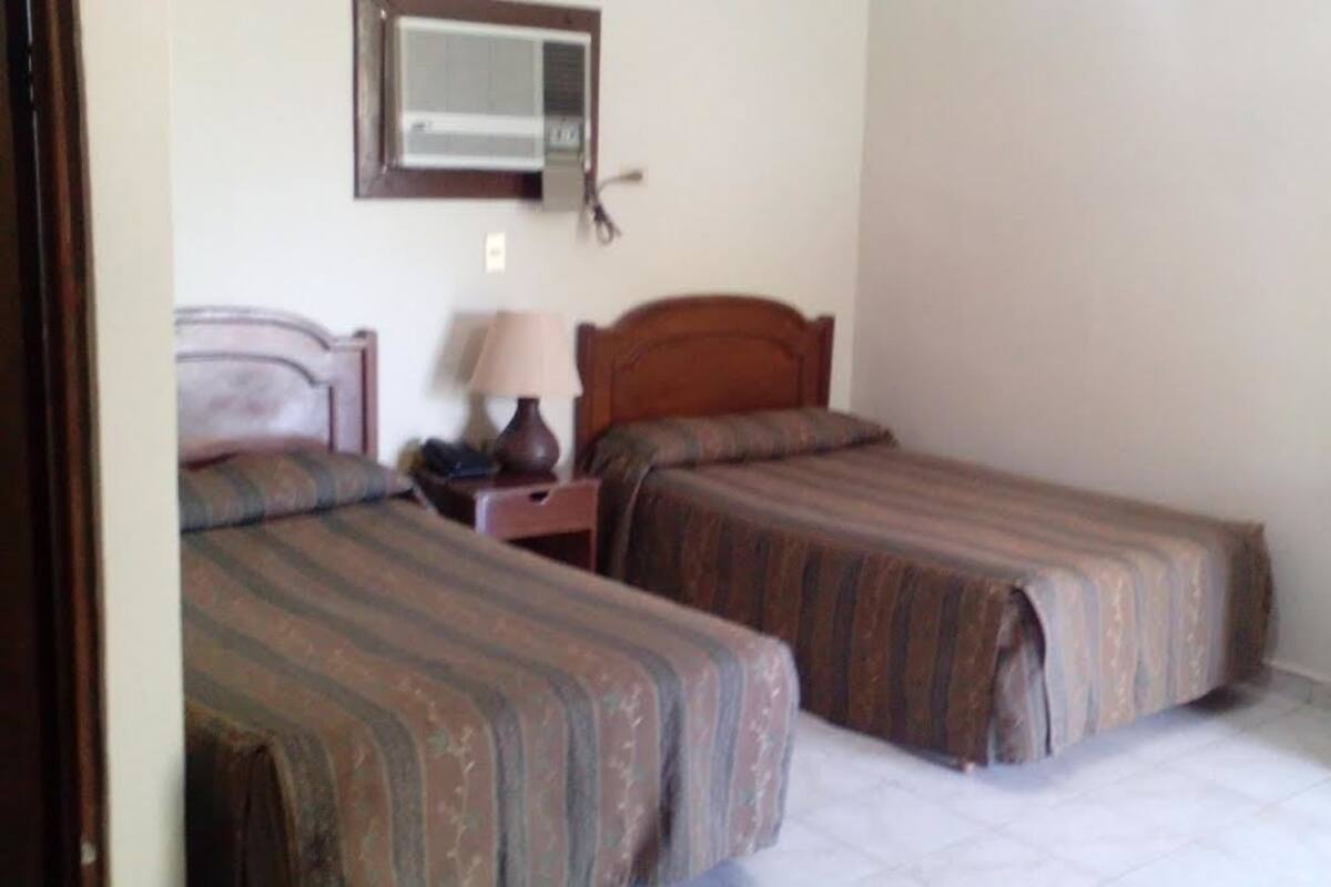 A bedroom with two single beds, a bedside table with a lamp, and a wooden nightstand.