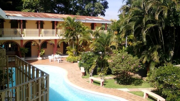 Un hotel con piscina, area salotto esterna e rigogliosa vegetazione.