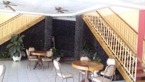 Zona pranzo con tavoli e sedie rotonde, una scala con ringhiera e una ventola a soffitto.