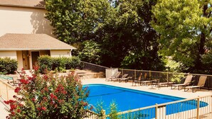 Una piscina con cubierta de madera y sillas reclinables, rodeada de vegetación y árboles.