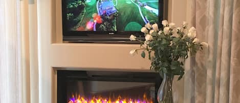 A flat-screen TV mounted above a fireplace with a vase of flowers on a pedestal.