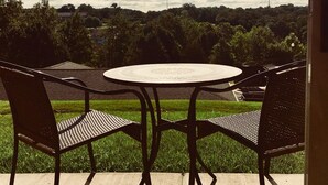 Un patio con una mesa redonda y cuatro sillas, con vista a un área verde y una vista distante de árboles y un edificio.