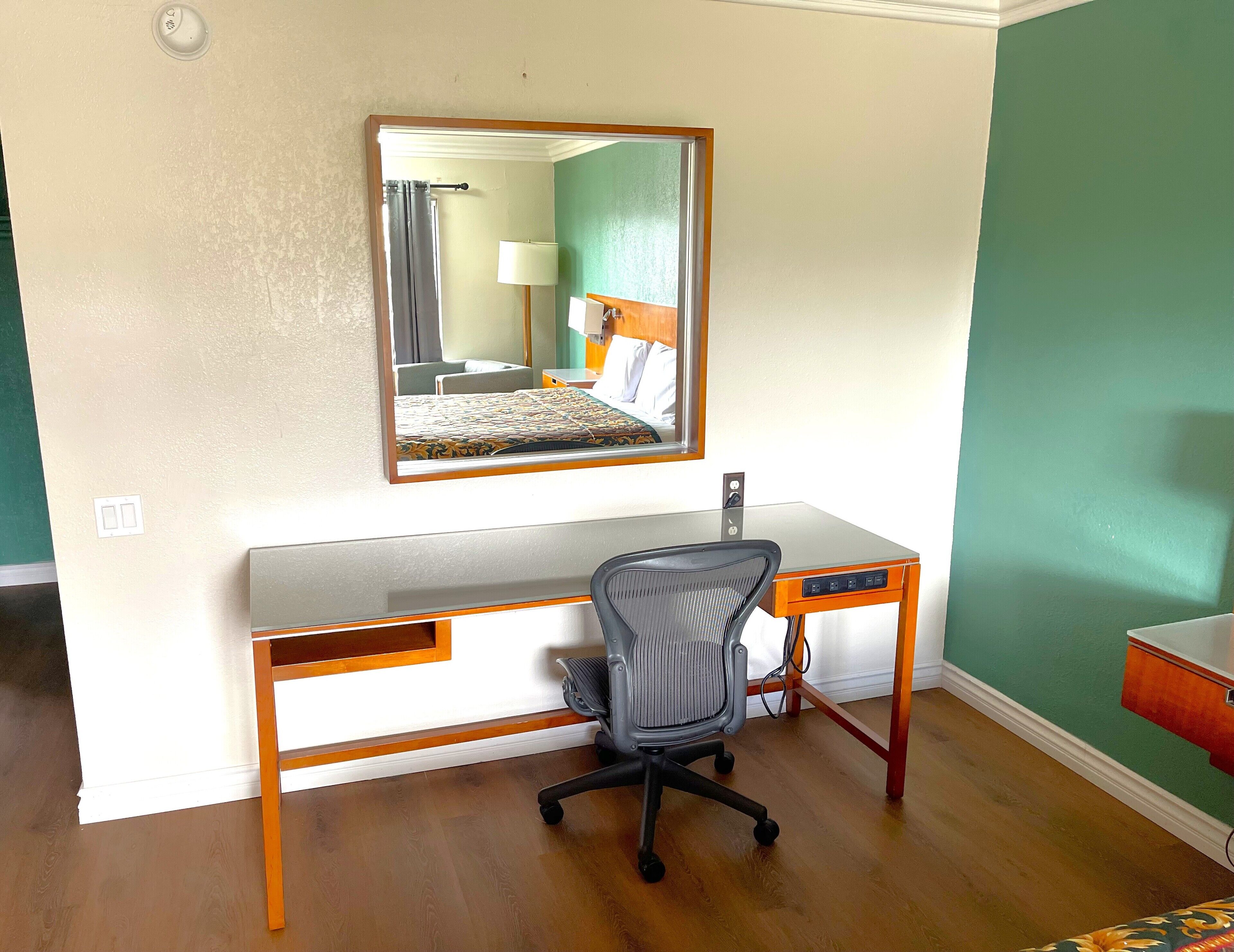 A hotel room with a desk, chair, and a large mirror.