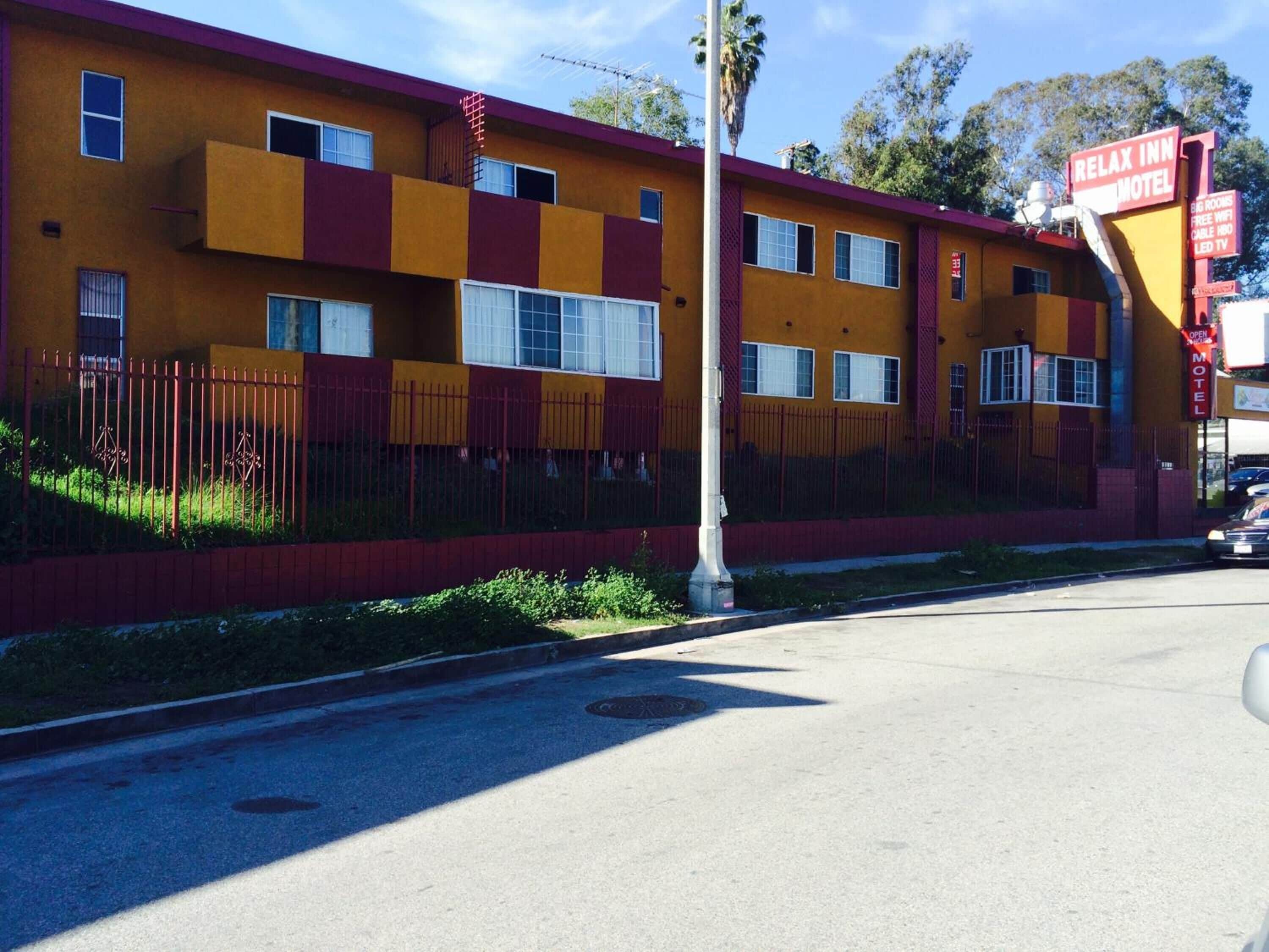 A motel with a yellow facade, multiple windows, and a red fence.