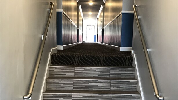 A modern hotel hallway with a patterned carpet, metallic handrails, and a view of the exit at the end. - Relax Inn Motel (Los Angeles)