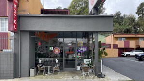 A motel with a glass storefront, outdoor seating, and a neon 'OPEN' sign. - Relax Inn Motel (Los Angeles)