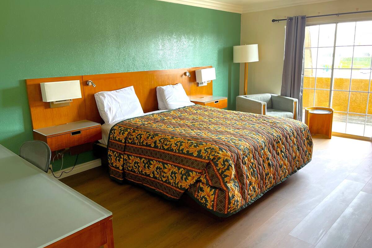A hotel room with a bed, bedside tables, a chair, a lamp, and a view of the outdoors.