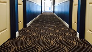 A hotel hallway with a patterned carpet, doors on both sides, and a light at the end. - Relax Inn Motel (Los Angeles)