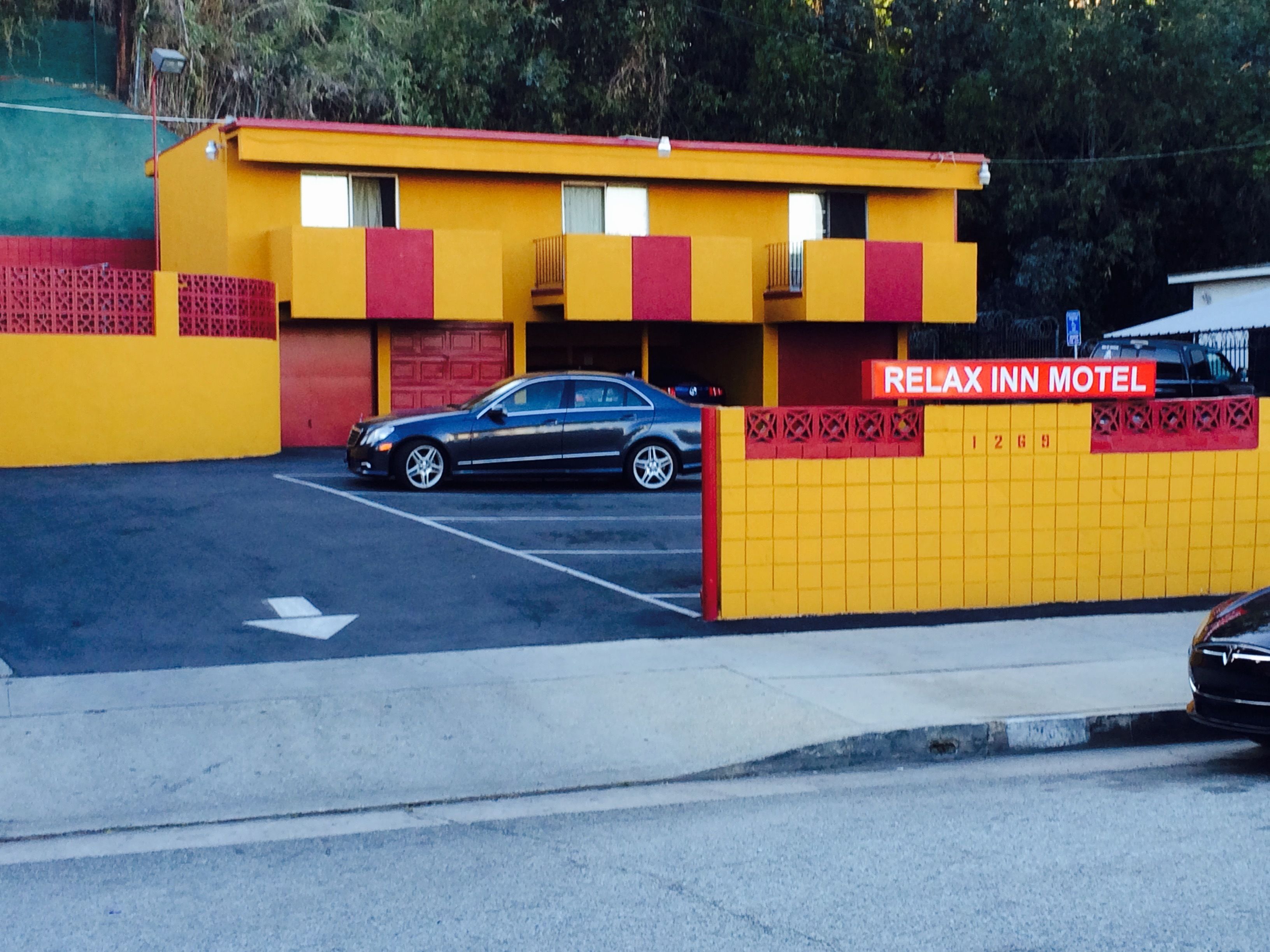 A motel with a yellow and red exterior, a parking lot, and a car parked in front.