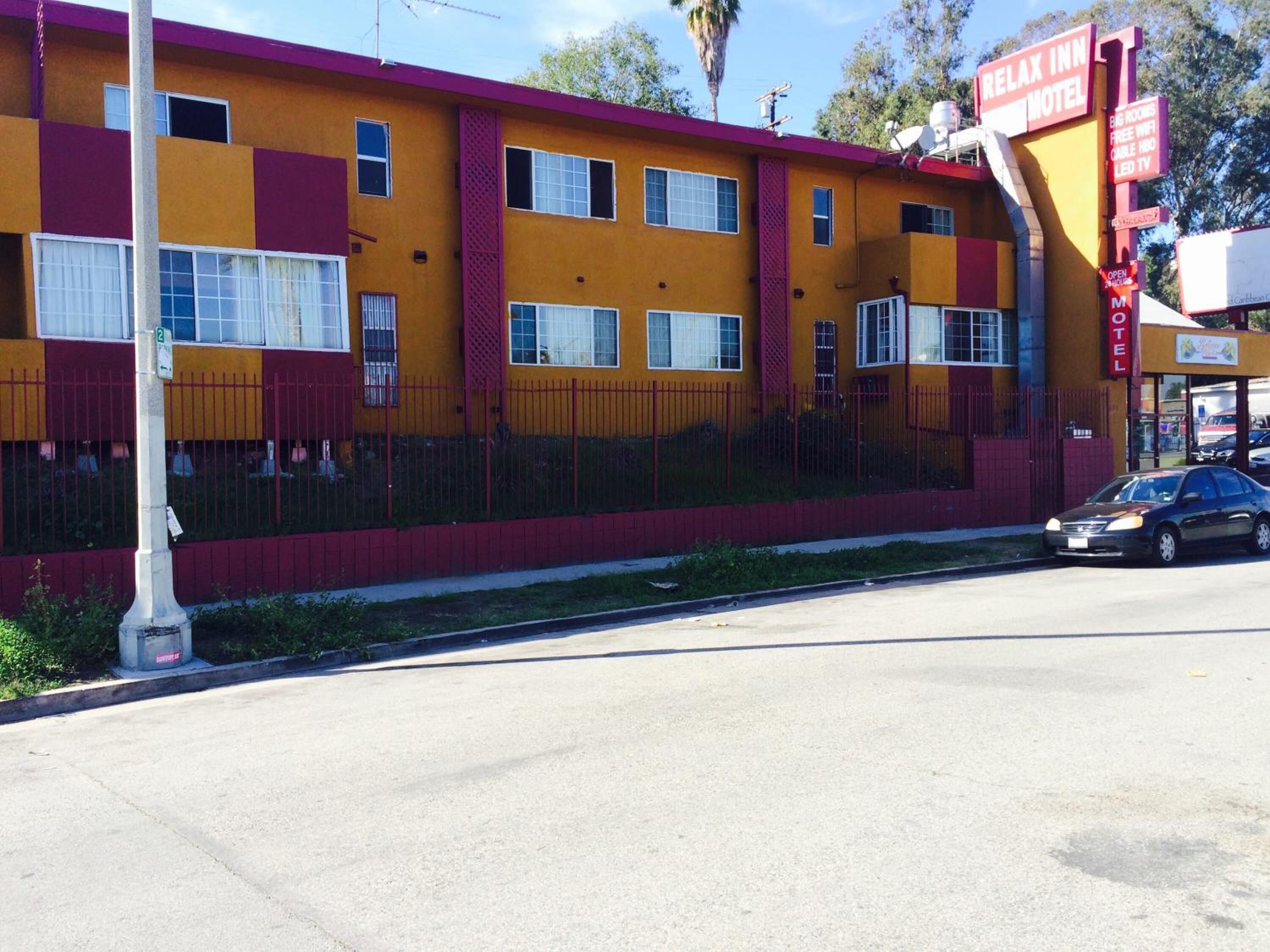 A motel with a yellow facade, red accents, and a sign indicating it is a 'Relax Inn Motel'.
