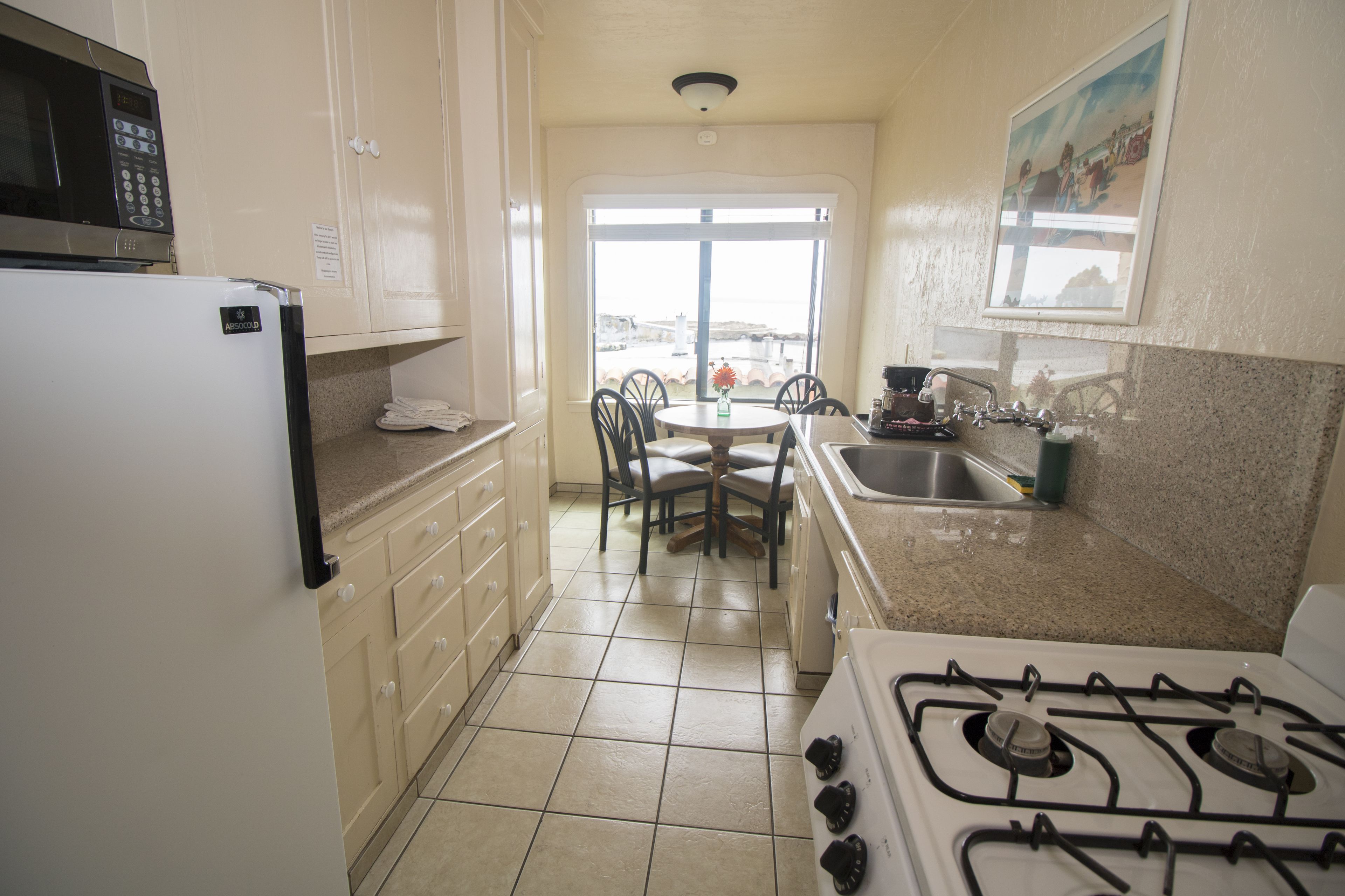 A kitchen with a refrigerator, stove, sink, and dining area with chairs and a table.