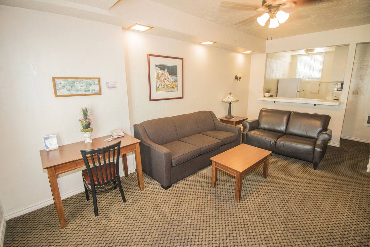 A living room with a brown sofa, a wooden coffee table, a dining table with chairs, and a small side table with a lamp.