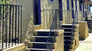 Une rangée de bâtiments en terre cuite, dotés de balcons, chacun étant accessible par un petit escalier menant à l’entrée.