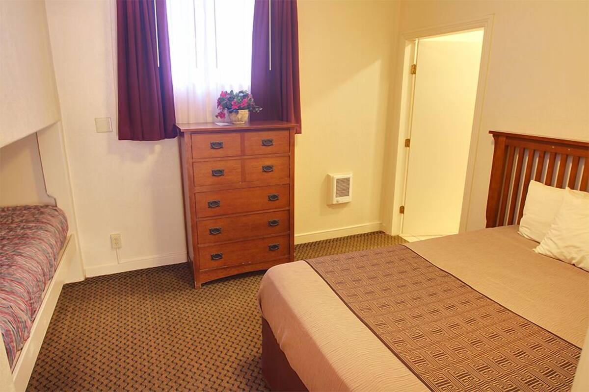 A bedroom with a single bed, a dresser, and a window with curtains.