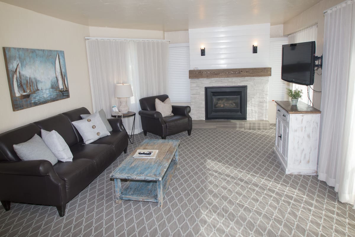 A living room with a sofa, armchair, coffee table, fireplace, TV, and a painting on the wall.