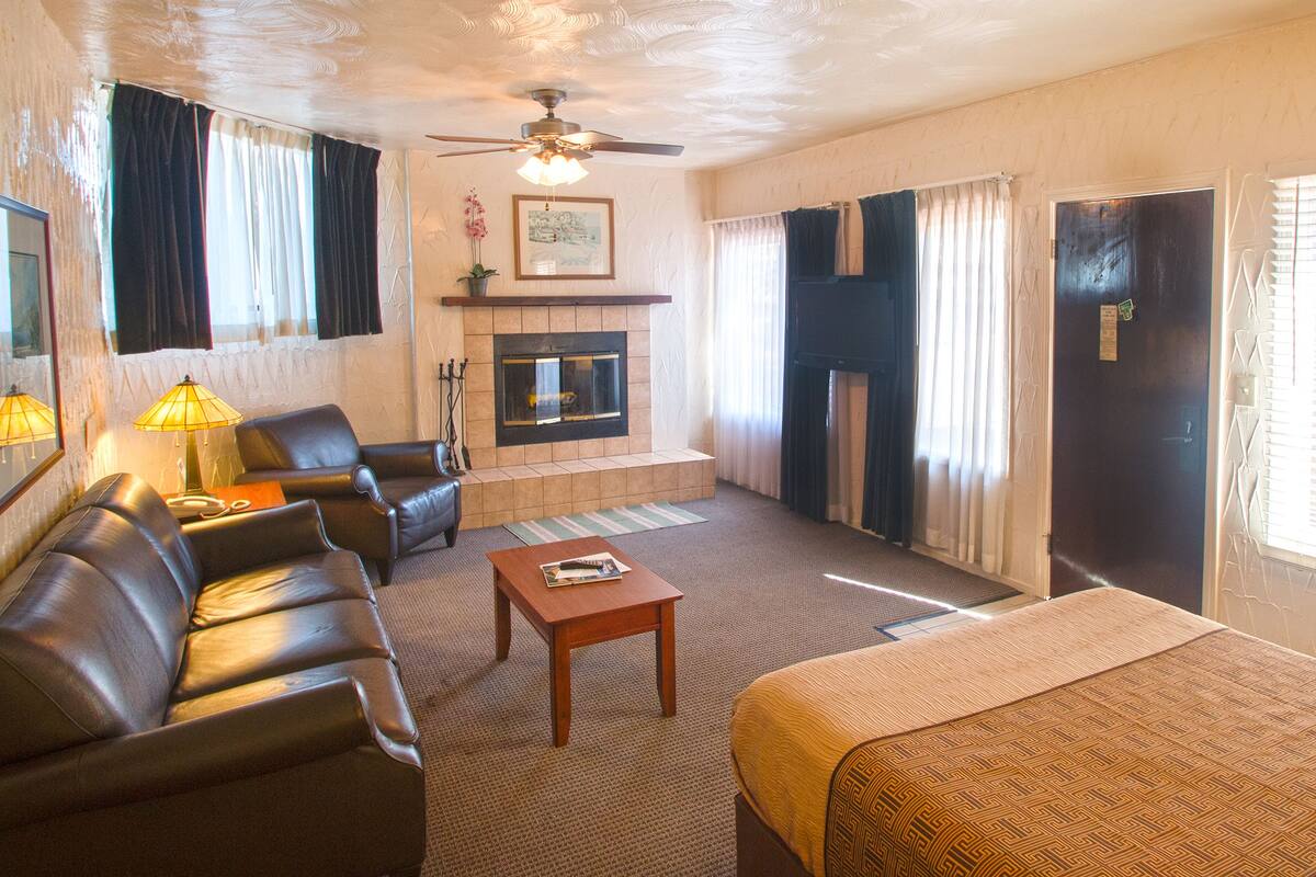 A living room with a fireplace, leather sofa, a coffee table, and a bed.