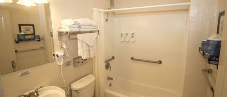 A bathroom with a sink, toilet, and bathtub. There are towels stacked on a shelf, a hand dryer, and a mirror.