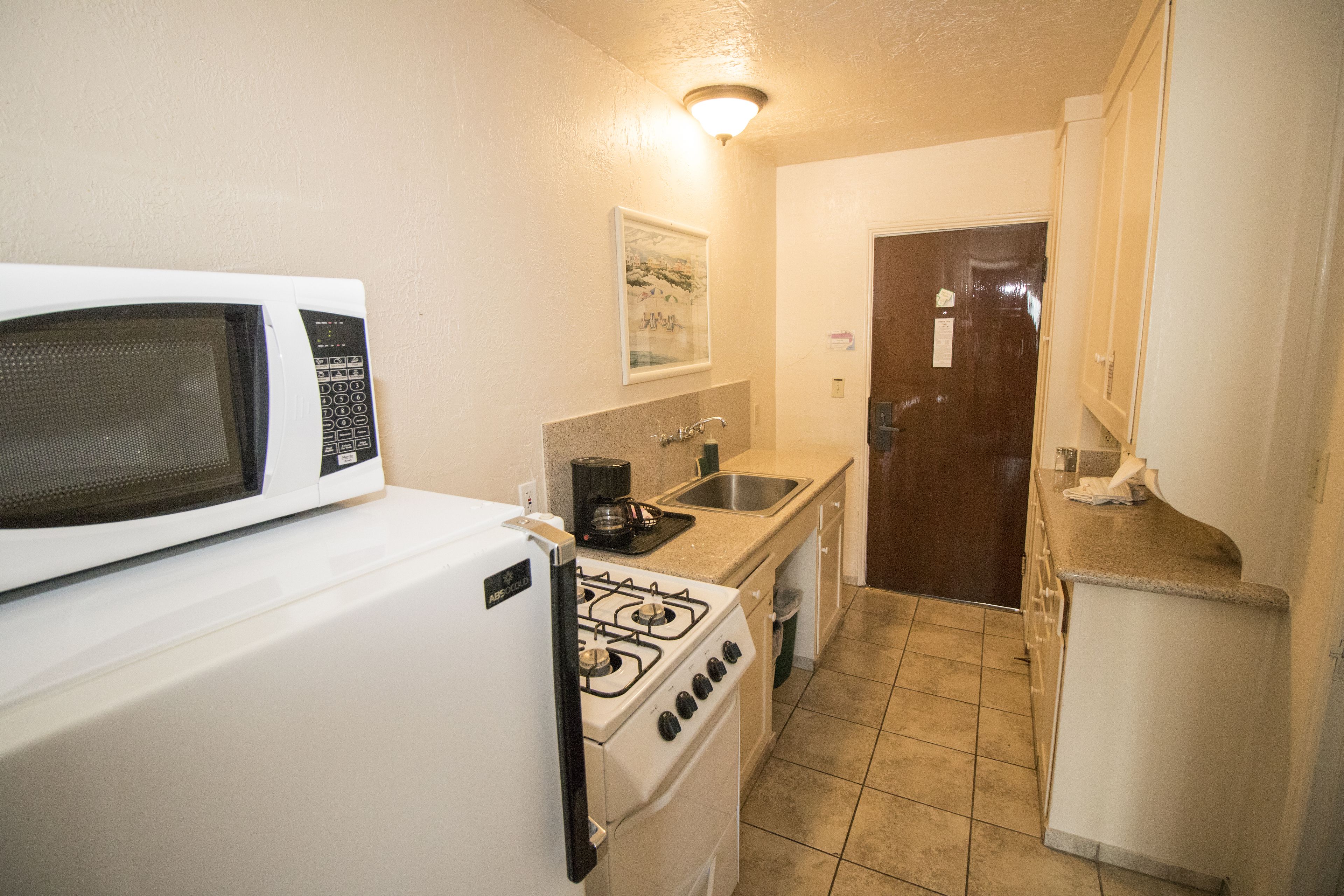 A compact kitchen with a white refrigerator, a microwave, a stove, a sink, and a small countertop.