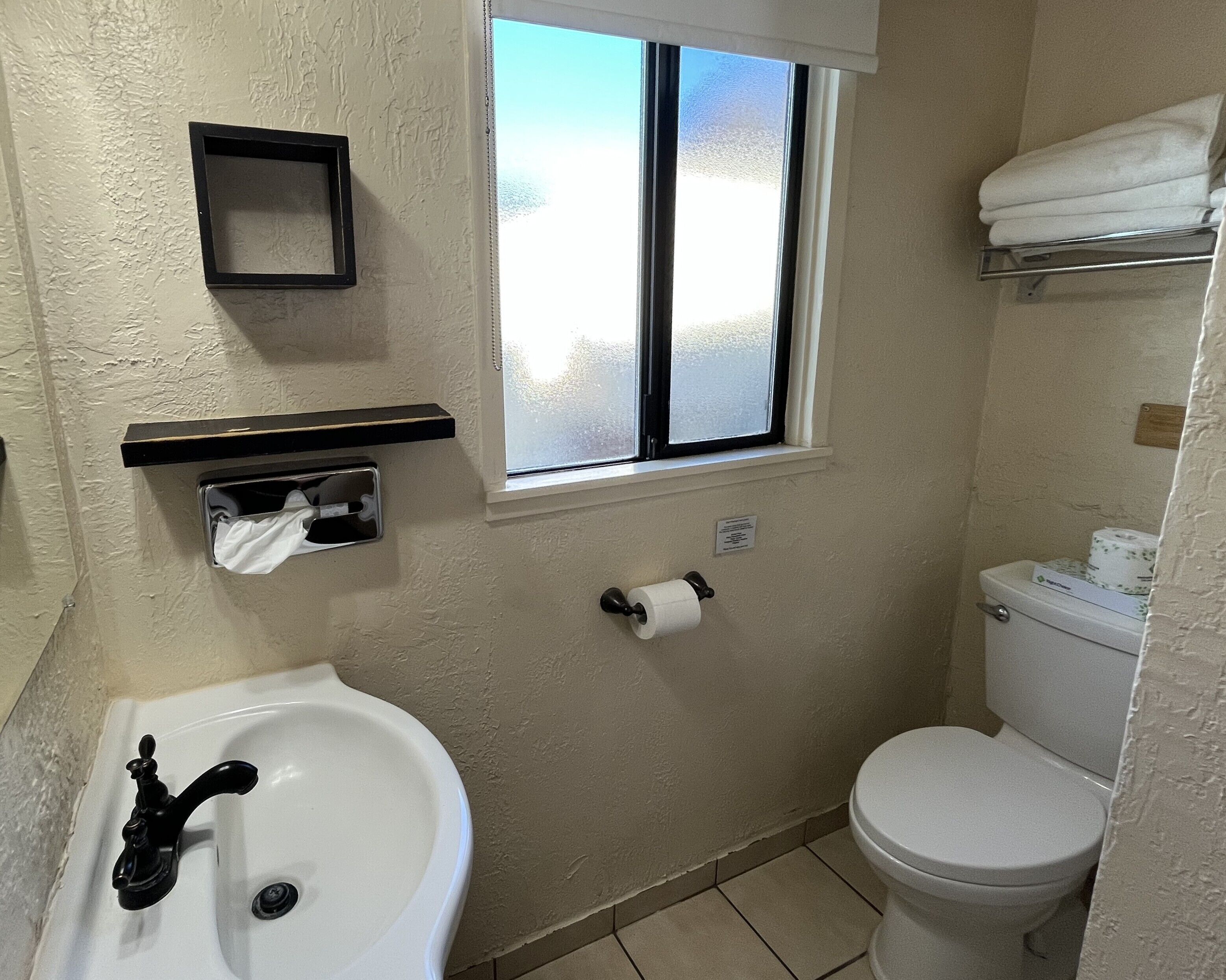A bathroom with a sink, toilet, window, and towel rack.