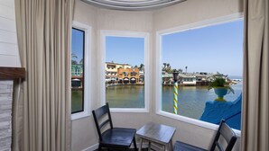 Une chambre d’angle dotée de deux fenêtres donnant sur une marina, comprenant un fauteuil, une petite table et une vue sur les bâtiments et l’eau.