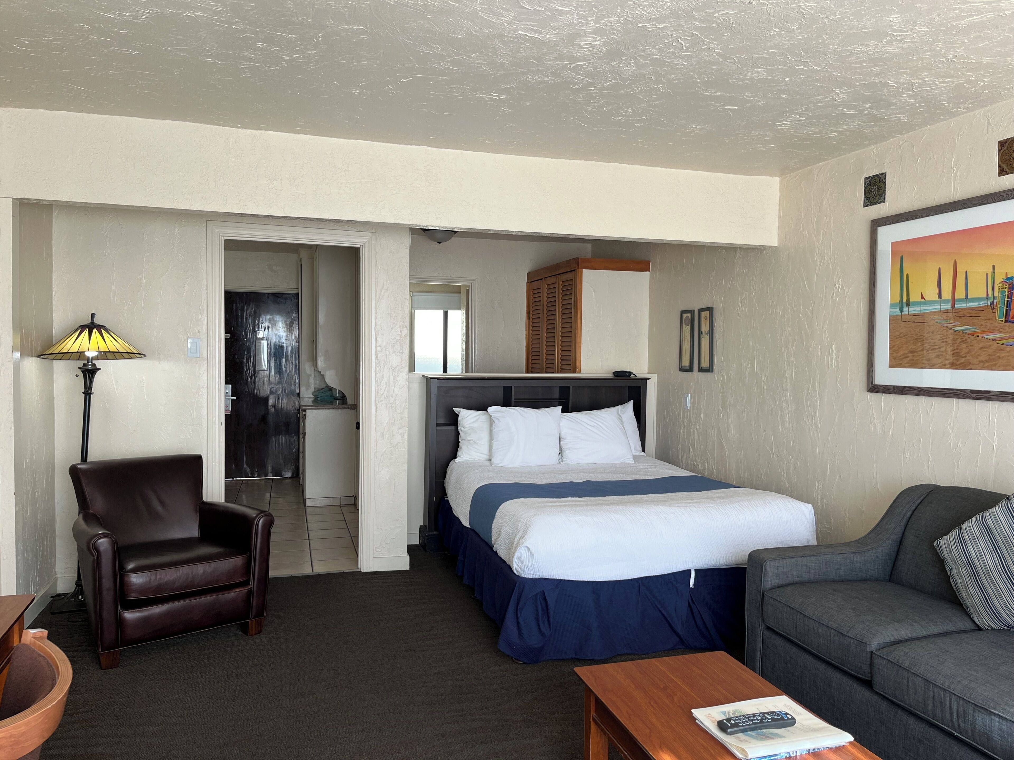 A hotel room with a bed, a chair, a sofa, a lamp, and a painting on the wall.