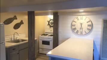 A kitchen with a large wall clock, a stove, and a sink.
