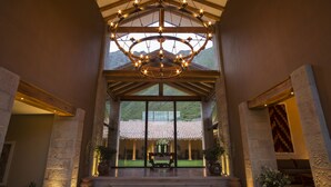 A grand entrance with a large chandelier, stone pillars, and a view of a traditional building through large glass doors. - Inkaterra Hacienda Urubamba (Huayllabamba)