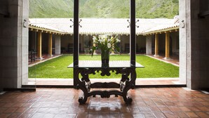 A courtyard with a glass table and chairs, surrounded by a building with a tiled roof and columns. - Inkaterra Hacienda Urubamba (Huayllabamba)