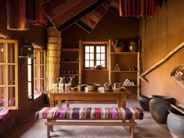 A rustic room with a wooden table, benches, and shelves filled with pottery and baskets.