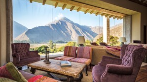 A cozy lounge area with a view of mountains, featuring plush seating and a wooden coffee table. - Inkaterra Hacienda Urubamba (Huayllabamba)