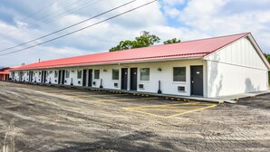 A motel with a red roof and white exterior walls, featuring a row of rooms with individual doors and windows, and a parking lot with marked spaces. - The Lake House Inn (Laurie)