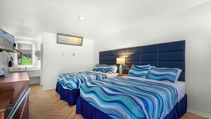 A bedroom with two beds, a wooden dresser, a window with a view, and a wall-mounted lamp. - The Lake House Inn (Laurie)