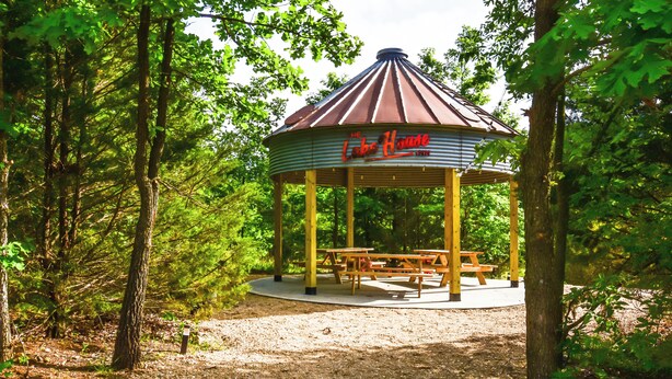 A gazebo with a roof supported by wooden pillars, surrounded by trees and a gravel path. - The Lake House Inn (Laurie)