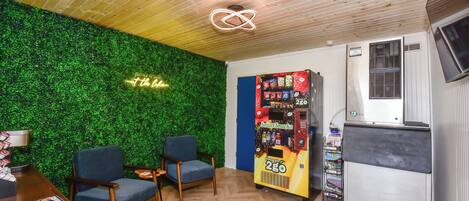 Una habitación con una pared verde, dos sillas azules, una máquina expendedora y un refrigerador pequeño.