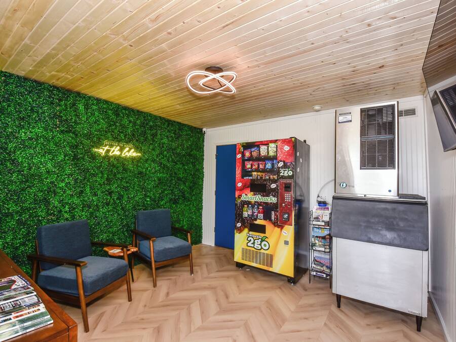 Habitació amb una paret verda, dues cadires blaves, màquina expenedora i un refrigerador petit.