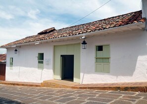 Un edificio blanco con techo de tejas, una puerta verde y dos ventanas con contraventanas.