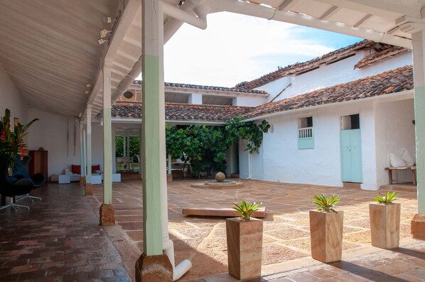 Un patio cubierto con suelo de baldosas, plantas en macetas y una zona de estar con mesa y sillas.