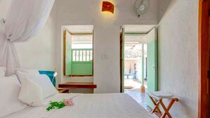 A bedroom with a bed, a bedside table, a window, and a door leading outside. - La Nube Posada (Barichara)