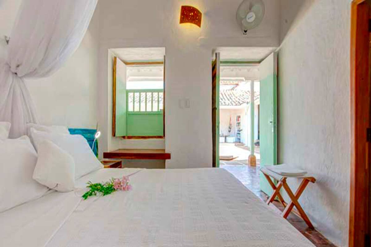 A bedroom with a bed, a bedside table, a window, and a door leading outside.