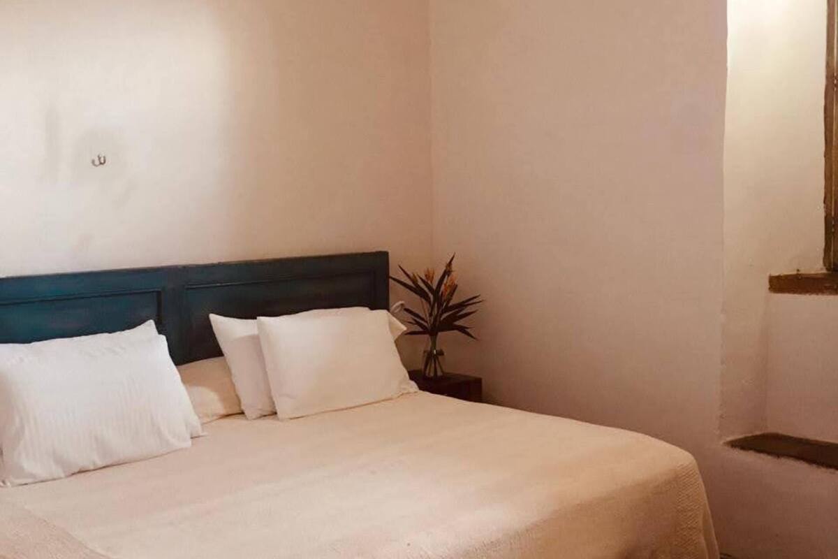 A neatly made bed with white linens, a wooden headboard, and a bedside table with a vase of flowers.