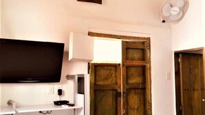 A room with a flat-screen TV on a white stand, a wooden door, and a white wall with a small square object. - La Nube Posada (Barichara)