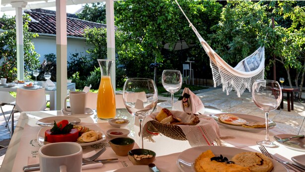 An outdoor dining area with tables set for breakfast, including plates of food, glasses of wine, and a hammock. - La Nube Posada (Barichara)