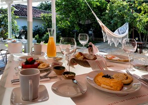 An outdoor dining area with tables set for breakfast, including plates of food, glasses of wine, and a hammock. - La Nube Posada (Barichara)