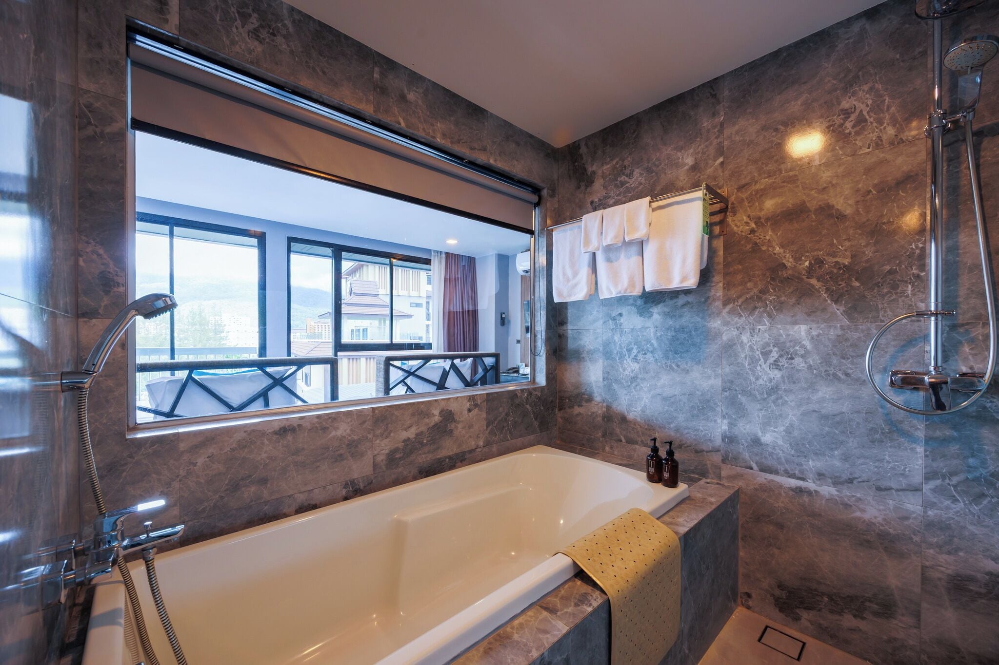 A modern bathroom with a large bathtub, a glass-enclosed shower, and a view through a large window.