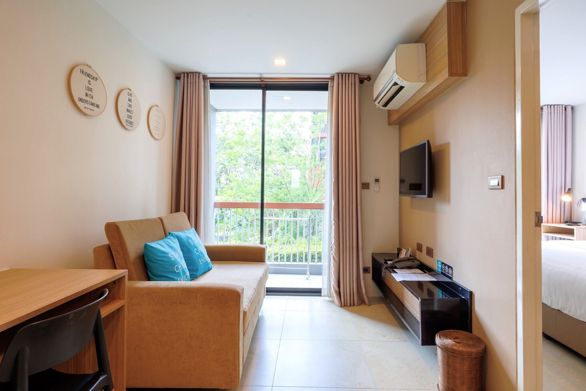 Habitación de hotel compacta con sofá, escritorio, televisión y balcón con cortinas.