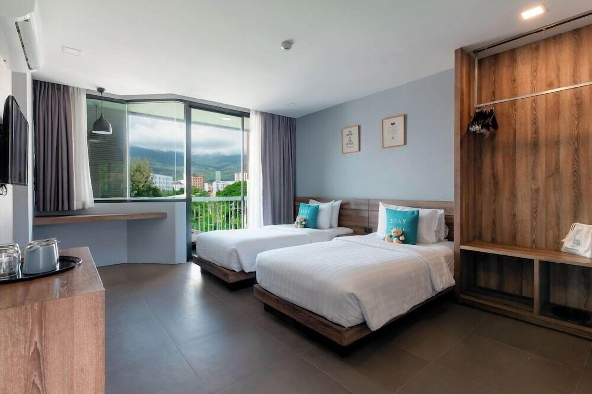Une chambre d’hôtel avec deux lits, une armoire en bois, une fenêtre donnant sur un beau paysage et un bureau avec une télévision.