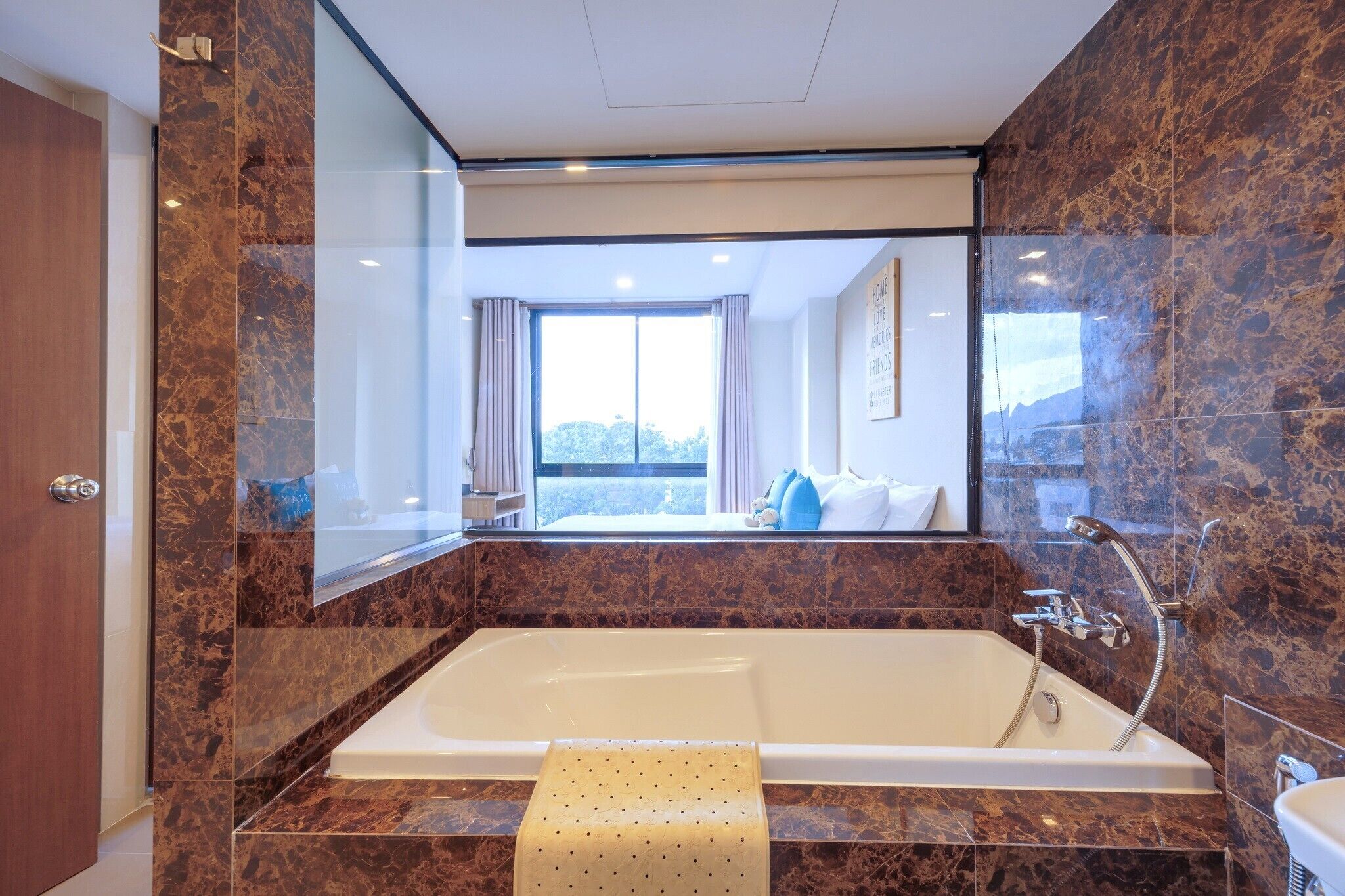 A modern bathroom with a large bathtub, marble walls, and a large mirror reflecting the room.